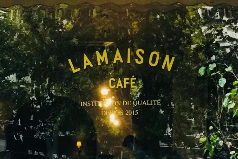 群青咖啡馆玻璃窗上的金色标识：LA MAISON CAFÉ，INSTITUTION DE QUALITÉ，DEPUIS 2015