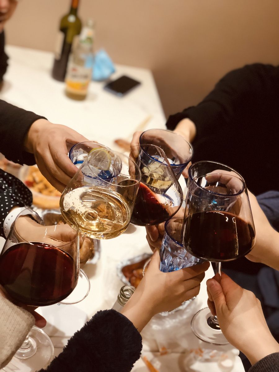 群青咖啡馆的聚会场景：多只手举着红酒杯与白葡萄酒杯碰杯，餐桌上有菜品与酒瓶